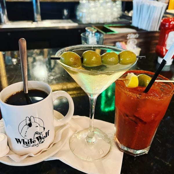 A White Wolf Cafe coffee mug, martini, and Bloody Mary on a bar counter.